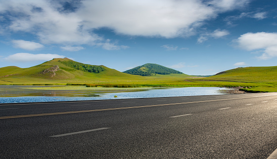 The endless grassland in spring and the forest hills in the distance beside the asphalt highway