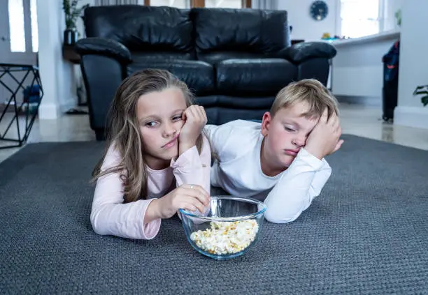 Coronavirus lockdow. Bored little girl and sad boy watching tv in isolation at home during quarantine COVID 19 Outbreak. Mandatory lockdowns and school closures impact on children mental health.