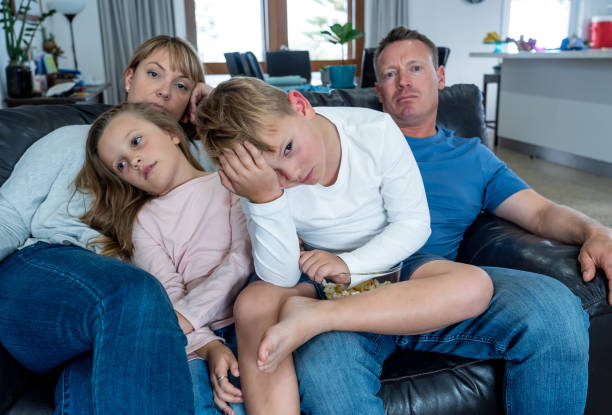 Coronavirus lockdow. Bored family watching tv helpless in isolation at home during quarantine COVID 19 Outbreak. Mandatory lockdowns and self isolation recommendations forces families stay home.