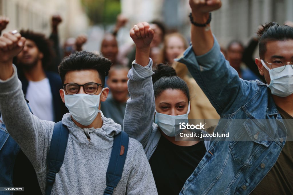 Group of demonstrators protesting in the city Group of people wearing face mask protesting and giving slogans in a rally. Group of demonstrators protesting in the city. Protest Stock Photo