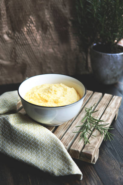 Creamy corn traditional polenta or mamaliga with butter. Served in white shallow dish on rustic wooden table with rosemary. Creamy corn traditional polenta or mamaliga with butter. Served in white shallow dish on rustic wooden table with rosemary. Country style. Selective focus, copy space, top view. Healthy food concept mamaliga stock pictures, royalty-free photos & images