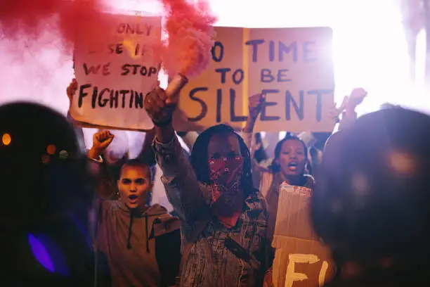 Protestors demonstrating with smoke bombs in front of police force at night. Anti-government protest by a group of social activists.