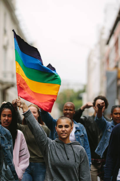 Supporters and members of LGBTQI community in a gay pride parade Female holding the gay rainbow flag at the Gay Pride Parade in city. Supporters and members of LGBTQI community during a Queer Pride Parade. peace demonstration photos stock pictures, royalty-free photos & images