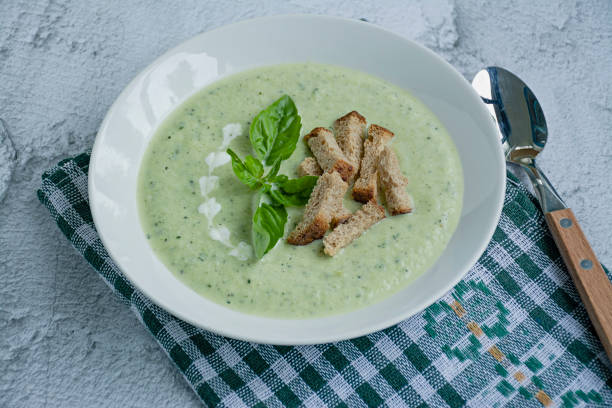 Zucchini puree soup and basil on a light background.