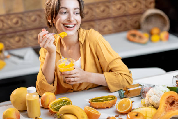 Woman eating chia pudding in the kitchen Young and cheerful woman eating chia pudding, having a snack or breakfast in the kitchen with lots of fresh fruits and vegetables. Concept of vegetarianism, healthy eating and wellness eating chia seeds stock pictures, royalty-free photos & images