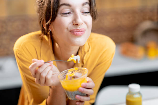 Woman eating chia pudding in the kitchen Portrait of a young and cheerful woman eating chia pudding, having a snack or breakfast in the kitchen. Concept of dieting, healthy eating and wellness eating chia seeds stock pictures, royalty-free photos & images