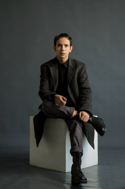 istock A young guy with a ponytail, in a classic grey coat and black leather military boots .Shooting in Studio on white cube, grey background. 1215073420