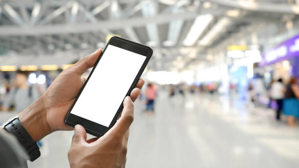 istock Smart man's hands holding a cropped black smartphone with white blank screen over crowded international airport as blurred background. 1215075984