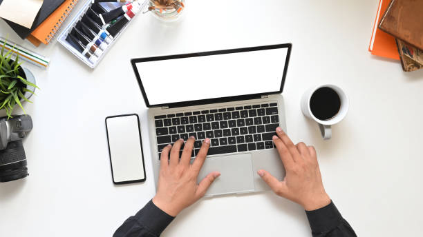 istock Top view Creative man's hands typing on computer laptop with white blank screen that putting on white working table surrounded with coffee cup, empty screen smartphone and accessories. 1215076030