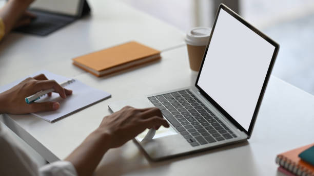 istock Cropped image of secretary woman's hands typing on computer laptop with white blank screen that putting on orderly working desk that surrounded with notes, coffee cup and stack of books. 1215076622