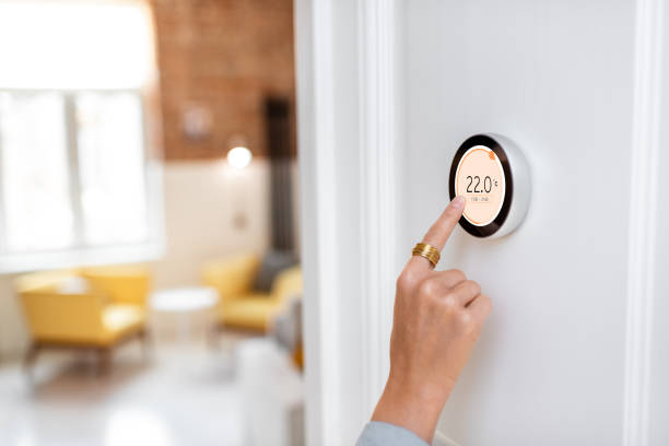 Regulating heating temperature with a modern wireless thermostat Woman regulating heating temperature with a modern wireless thermostat installed on the white wall at home. Cropped view focused on hand thermostat photos stock pictures, royalty-free photos & images