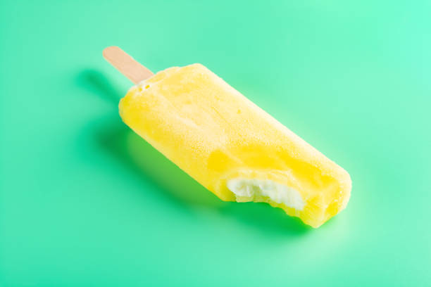 istock yellow popsicle with a big bite on a light green background 1215081299