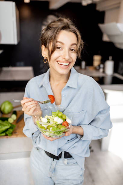 kobieta ze zdrową sałatką w kuchni - vegan food cheerful vertical indoors zdjęcia i obrazy z banku zdjęć