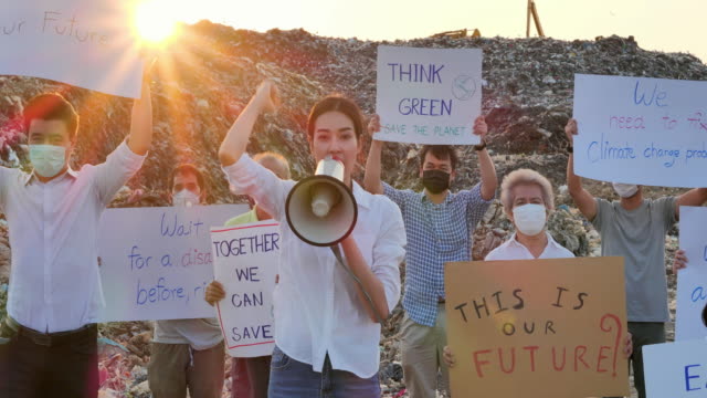 Asian leadership women shouting on megaphone of group asian volunteers of different age on a huge garbage dump from landfill site in Asia and holding posters for Environmental movement activists fighting for nature.Volunteerism, Charity, Cleaning, Ecology