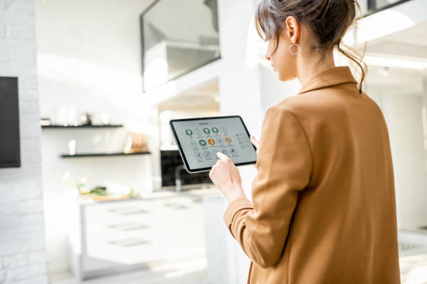 Controlling smart home with a digital tablet Woman controlling smart home devices using a digital tablet with launched application in the white living room. Smart home concept link house stock pictures, royalty-free photos & images