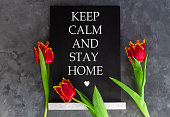 Words Keep Calm And Stay Home on chalkboard on grey concrete background with fresh tulips. Motivation banner text