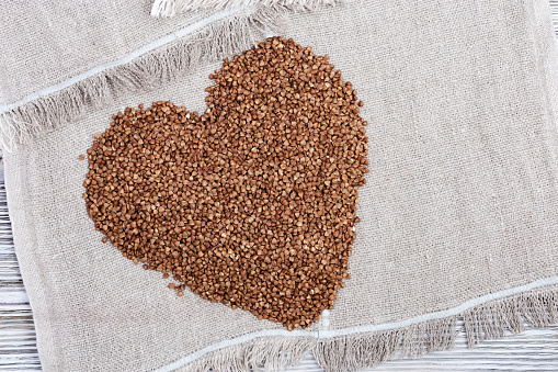 Raw roasted buckwheats in shape heart on light wood. Russian grechka. Organic healthy diet food.