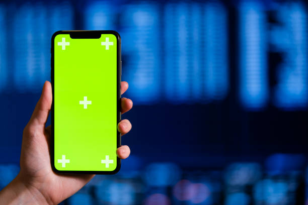 Close up of female hands using smartphone with green screen mobile phone for graphic display montage on a background of the digital monitor