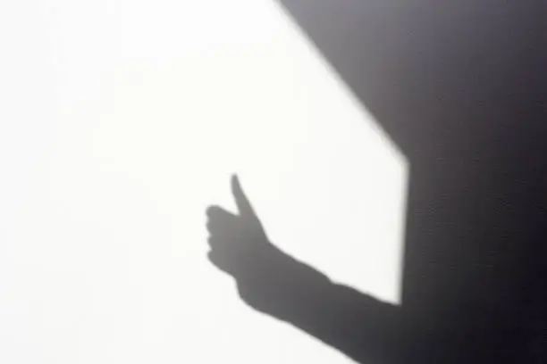 Photo of silhouette shadow hand doing tumbs up on white wall, isolated in home