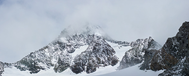 Scenery of rocky mountain Grossglockner, covered with snow. Panoramic view of snow-capped alpine rocks with pyramid-shaped peak under foggy sky. Concept of rocky hills, nature beauty and wintertime.