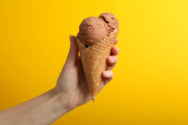 istock Female hand holds ice cream on yellow background, space for text 1215093501