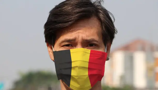 Photo of Belgium flag on hygienic mask. Masked man prevent germs. concept of Tiny Particle protection or virus corona.