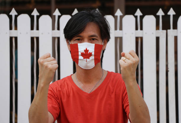Canada flag on hygienic mask. Masked the man prevent germs. Tiny Particle or virus corona or Covid-19 protection. Lift the fist up for meaning fighting or concept of Combating illness.