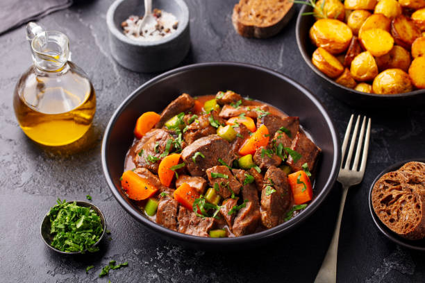 Beef meat and vegetables stew in black bowl with roasted baby potatoes. Dark background. stock photo