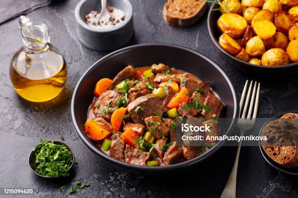 Beef Meat And Vegetables Stew In Black Bowl With Roasted Baby Potatoes Dark Background Stock Photo - Download Image Now