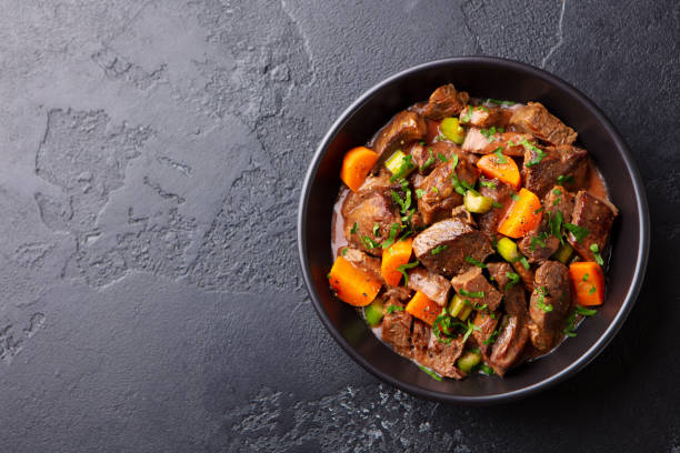 istock Beef meat and vegetables stew in black bowl. Dark background. Copy space. Top view. 1215096347