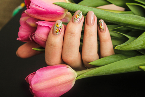 Spring manicure with a floral hand drawn design on the nails covered with beige gel Polish on the beautiful cancers of a young woman