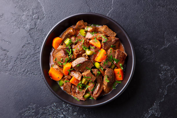Beef meat and vegetables stew in black bowl. Slate background. Top view. Beef meat and vegetables stew in black bowl. Slate background. Top view. beef stew stock pictures, royalty-free photos & images