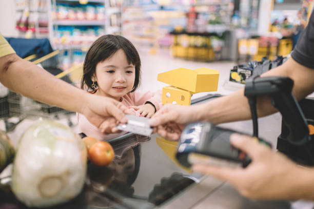 スーパーマーケットでカウンターチェックアウトでレジに彼の買い物品のために支払うアジアの中国の高齢者 - supermarket sales clerk grocer apron ストックフォトと画像