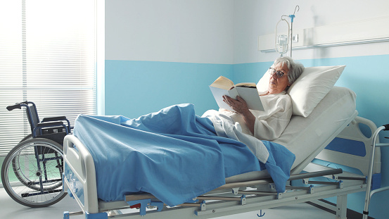 Senior woman lying in bed at the hospital and reading a book