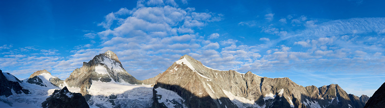 New day in the Swiss Alps at Dent Blanche, morning bright sun is shining at the ridge of rocky mountains, while the valley is still in the shadow, panoramic shot