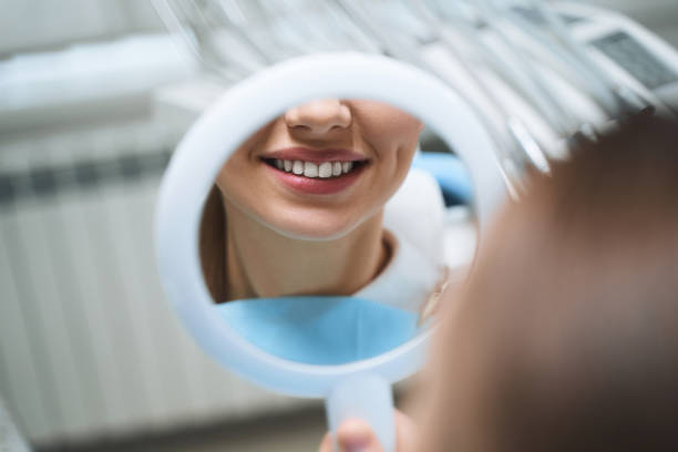 Woman with mirror at dentist stock photo Cheerful young girl is visiting dental clinic and looking at reflection of her smile after treatment tooth whitening photos stock pictures, royalty-free photos & images