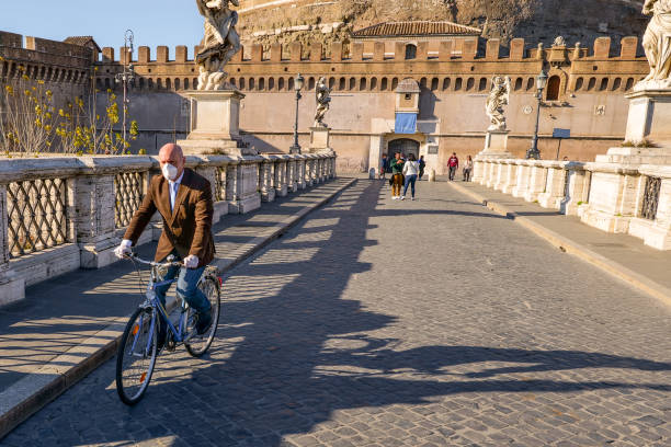 医療マスクを持つサイクリストは、ロックダウンのためにほとんどさびれたポンテ・サンタンジェロを横切ります - ponte sant angelo ストックフォトと画像