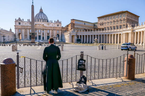 A Catholic priest prays on the edge of St. Peter's Basilica Square closed to tourists due to the Covid-19 lockdown Vatican, Italy, March 11 -- A Catholic priest prays in front of the square of St. Peter's Basilica deserted and closed to visitors and tourists for the lockdown. church of san pietro photos stock pictures, royalty-free photos & images