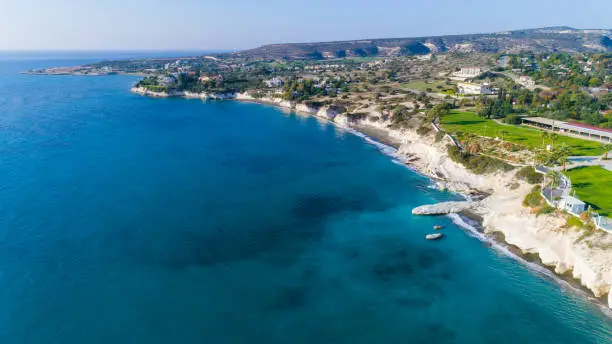 Aerial view of coastline and landmark big white chalk rock at Governor's beach, Limassol, Cyprus. The steep stone cliffs and deep blue sea waves crushing in coves and dark sand next to Kalymnos fish restaurant from above.