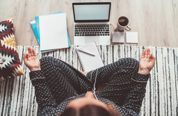 businesswoman dressed in pajamas, listening earphones meditating with morning coffee with gyan mudra palm on floor office with laptop, papers top view shot. distance work in quarantine time concept. - yoga business women indoors imagens e fotografias de stock