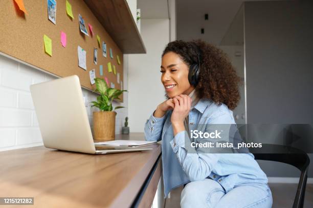 Smiling Young African American Teen Girl Wear Headphones Video Calling On Laptop Happy Mixed Race Pretty Woman Student Looking At Computer Screen Watching Webinar Or Doing Video Chat By Webcam Stock Photo - Download Image Now
