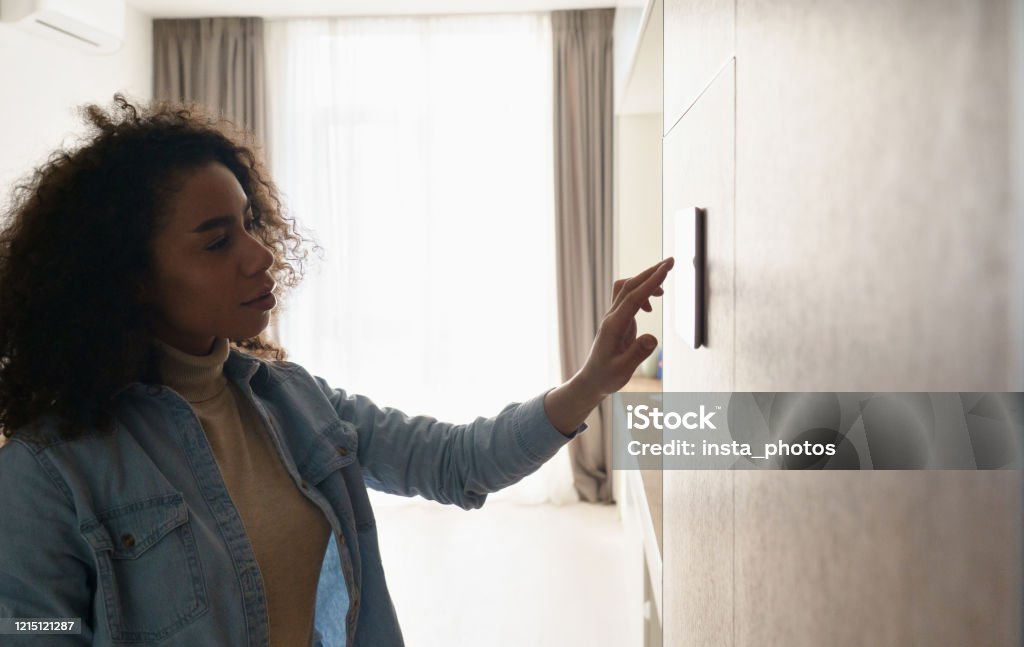 Joven africana mujer señora ajuste de la configuración del panel de control de clima remoto ajustes de la pared táctil pantalla táctil ajuste de calefacción interruptor de acondicionamiento en el modo de ahorro de energía del sistema de seguridad, ne - Foto de stock de Casa libre de derechos Joven africana mujer señora ajuste de la configuración del panel de control de clima remoto ajustes de la pared táctil pantalla táctil ajuste de calefacción interruptor de acondicionamiento en el modo de ahorro de energía del sistema de seguridad, ne - Foto de stock de Casa libre de derechos