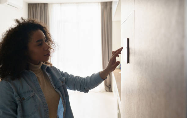 istock Young african girl woman lady adjusting remote climate control panel settings wall touch screen set heating conditioning switch on security system energy saving mode, black lady use smart home concept. 1215121287