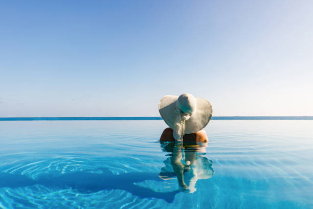 vista posteriore di una donna con cappello da sole nella piscina a sfioro. - infinity pool foto e immagini stock