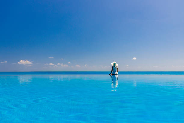 vista sul retro di una donna che guarda la vista sul mare da una piscina a sfioro. - infinity pool foto e immagini stock