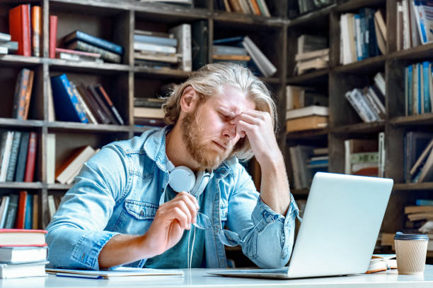 Young stressed tired man student worker library take off glasses feel pain rub closed eyes tired of computer screen studying work suffer from sore eyes syndrome headache have vision problems concept