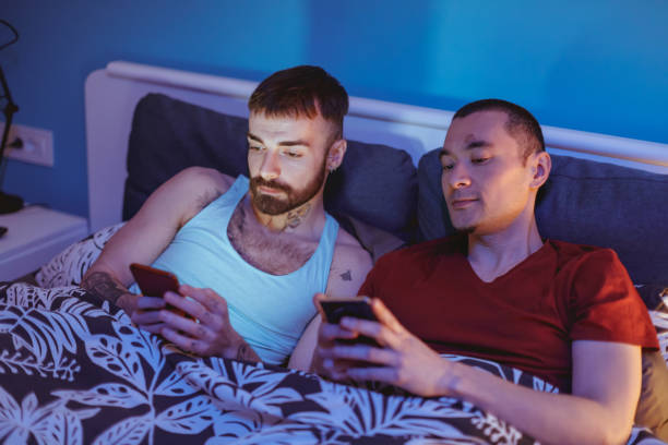 istock Gay couple using smartphones in bed, leaning on headrest 1215137420
