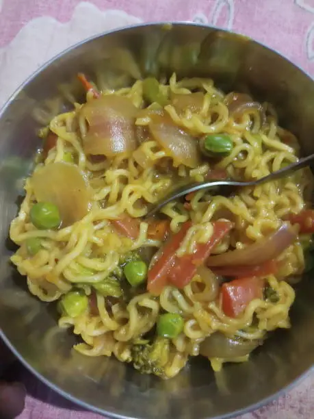 Homemade maggi with nice recipe with green motor,carrot,onion in a steel bowl.