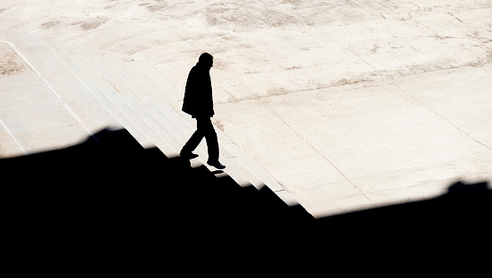 Shadow silhouette of a man walking alone down city stairs in sepia high angle view