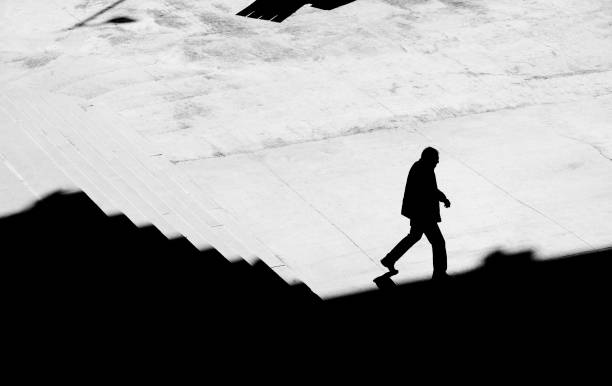 istock Shadow silhouette of a man walking alone down city stairs 1215138601